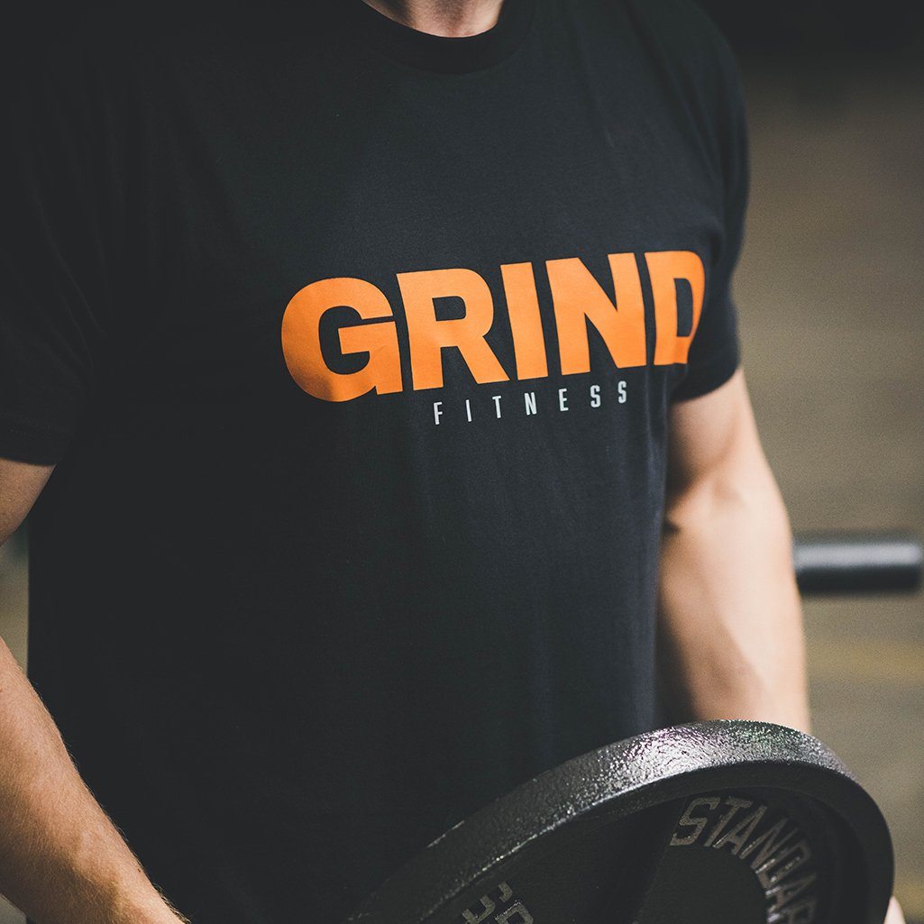 Angled The GRIND Fitness Black Tee Shirt with Orange and Grey Logo chest print.