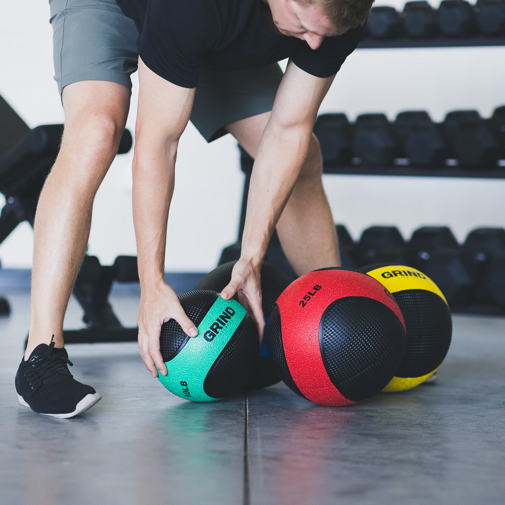 Man reaching to pick up green Medicine Ball from floor. 