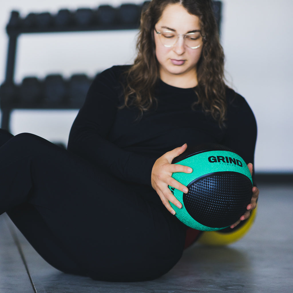 Woman sitting on floor performing a Russon Twist with green Medicine ball.