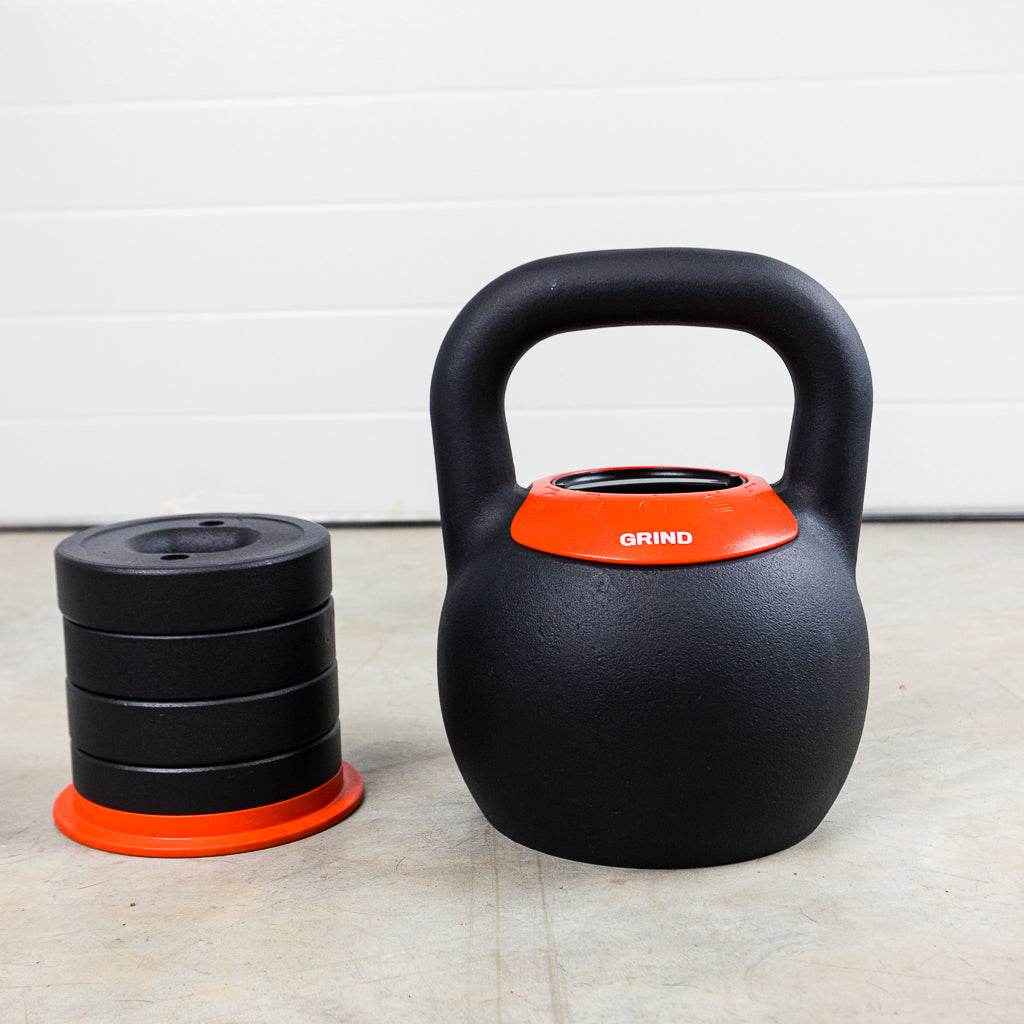 GRIND Adjustable Kettlebell on the floor with a stack of weights that get inserted into kettlebell for various weights.
